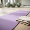 Lichtpaarse yogamat naast een handdoek in een rustige fitnessruimte