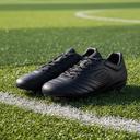 Zwarte voetbalschoenen naast een grasveld bij daglicht
